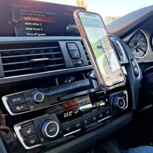 A smartphone displaying GPS navigation securely attached to a custom magnetic CD slot mount in a BMW dashboard.